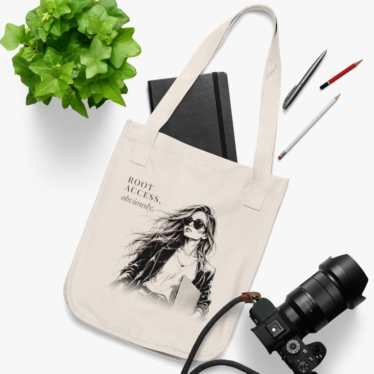 The tote laid flat with a black notebook, pens and a camera